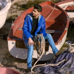 Mand i blå regnjakke med logo sidder på en båd